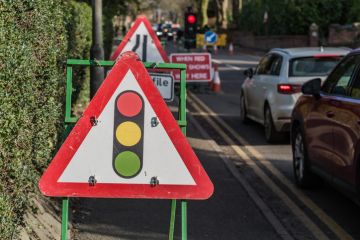 Traffic light road ahead sign against cars in the background.