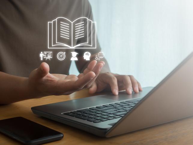 A virtual illustration of a book guides a student working on a laptop